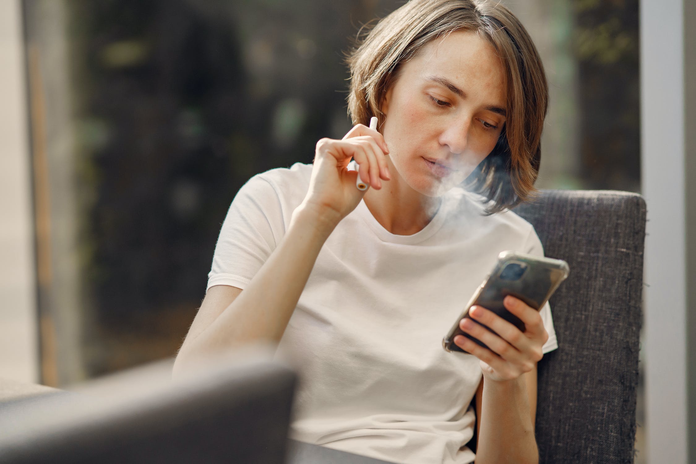 Woman smoking a vape while holding her phone